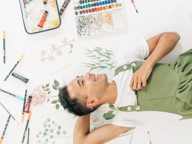 An artist photographed from above, lying among their paints and brushes