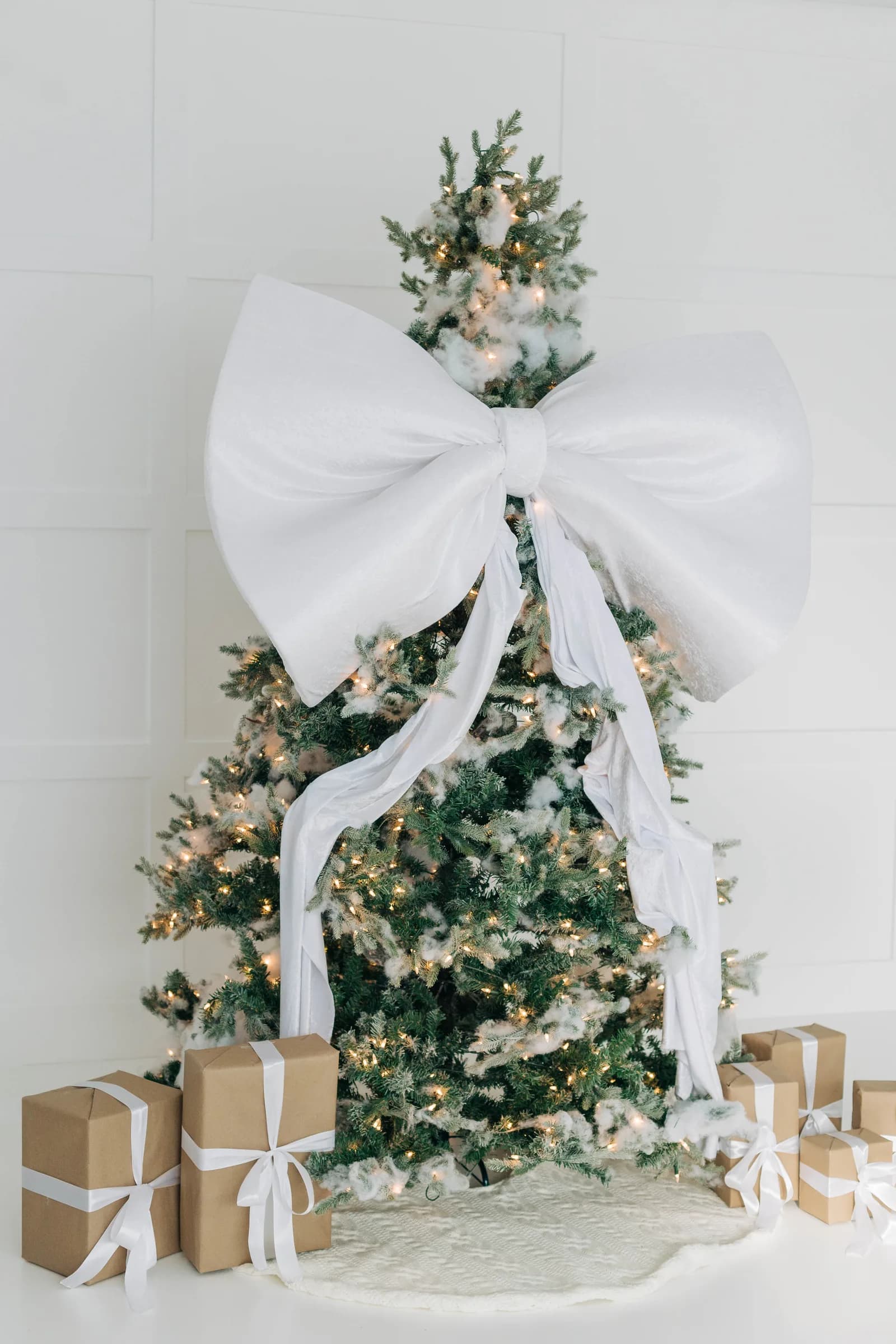 The white bow Christmas tree from the side, presents spread across the white studio floor in soft daylight