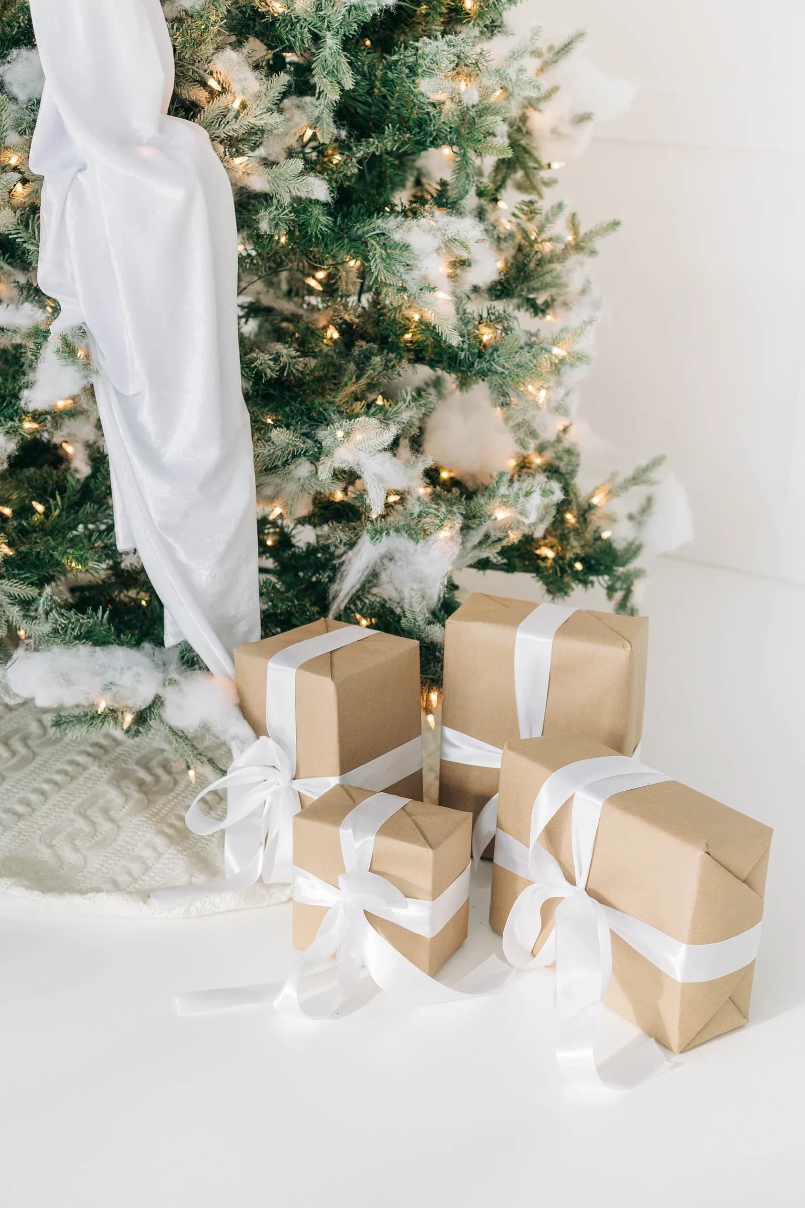Kraft paper presents tied with white satin bows tucked against the base of the flocked tree