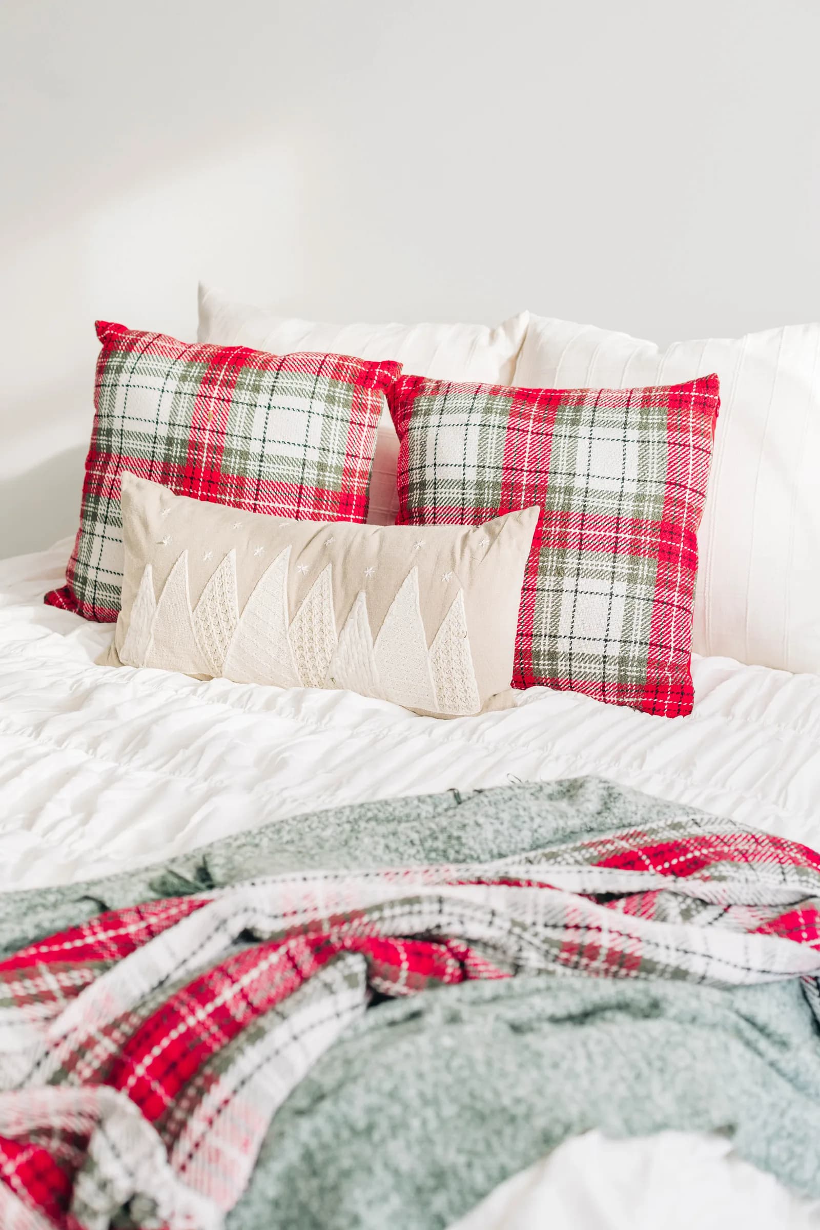 The holiday bed from an angle, plaid pillows against ruched white bedding in window light