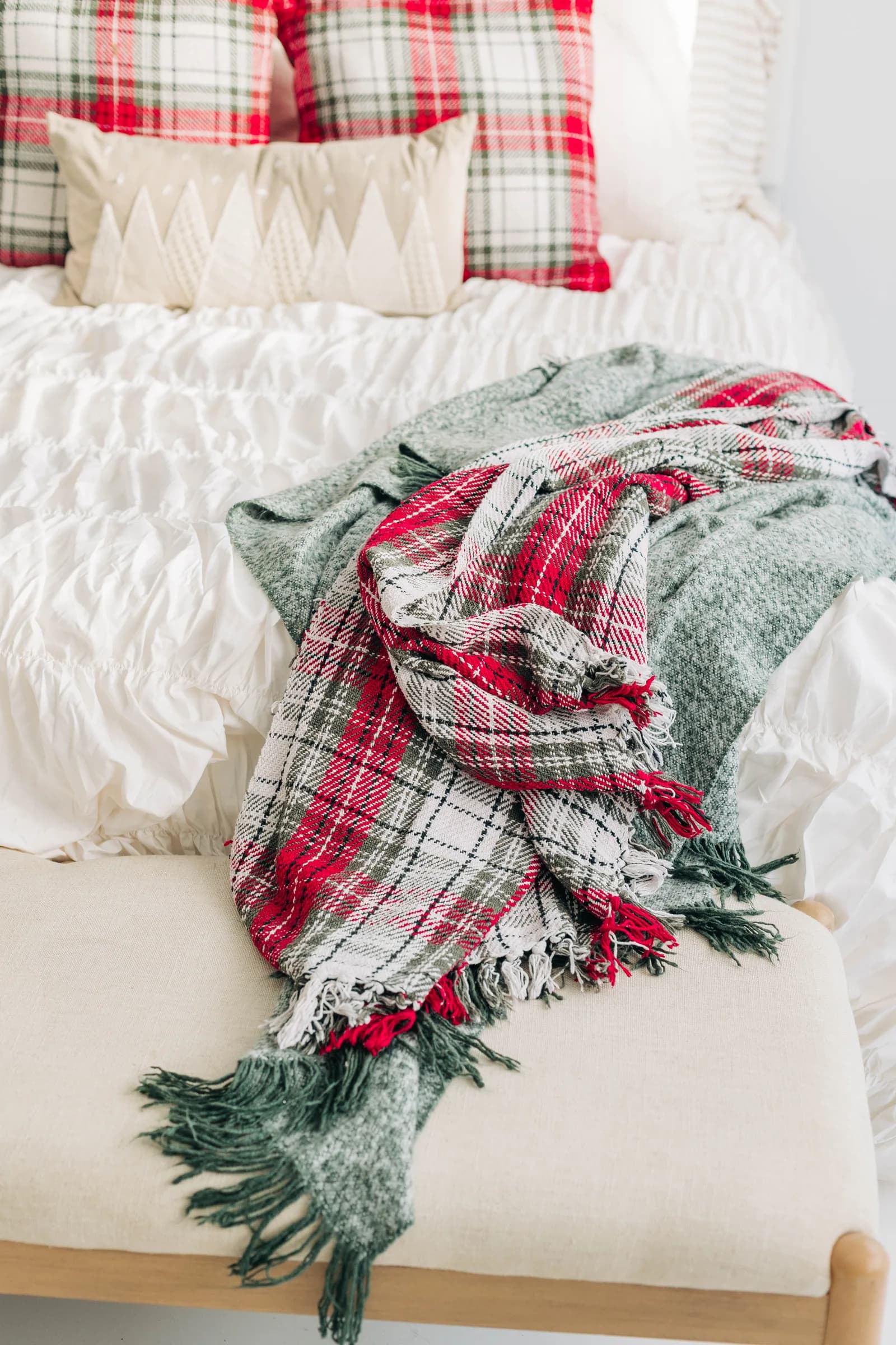 A red plaid throw and sage knit blanket draped over the foot of the holiday bed