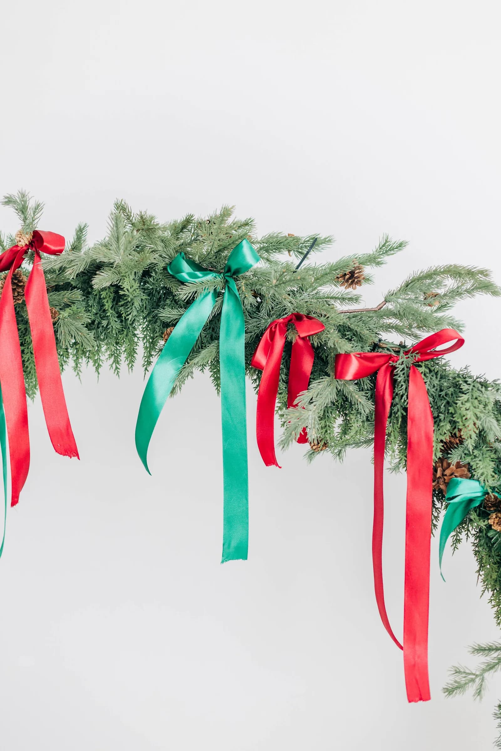 Red and green satin ribbons tied along a pine garland against a bright white wall