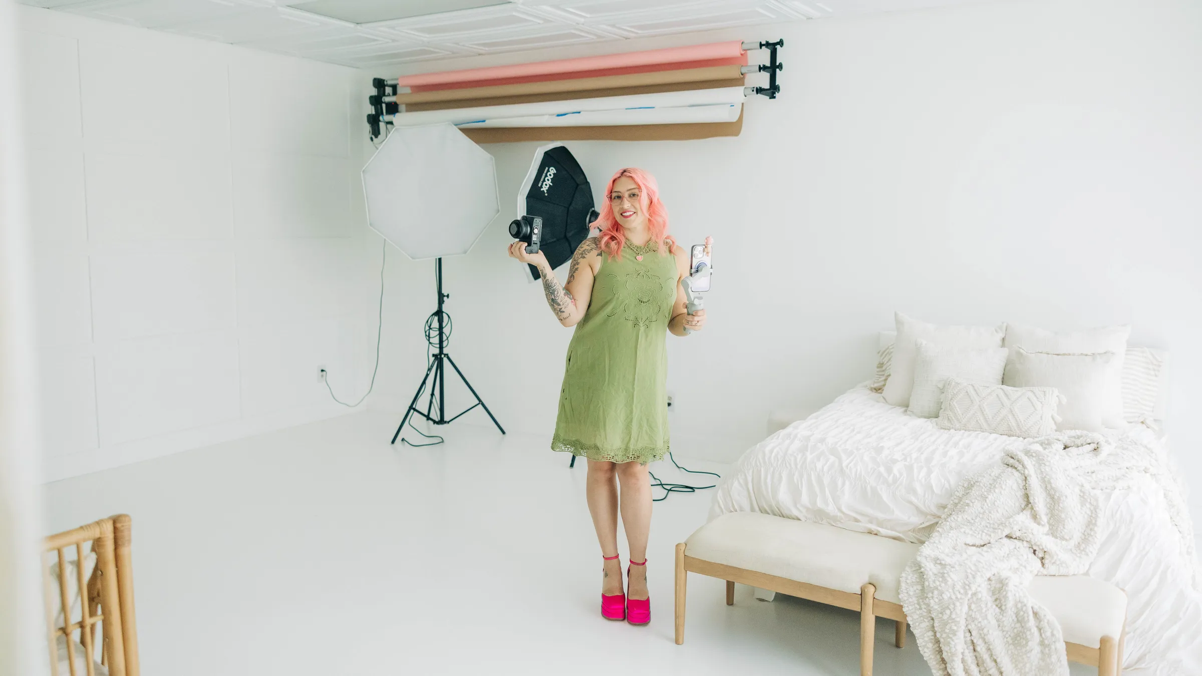 Sydney, camera in hand, in Studio A with the backdrop rack and styled bed behind her
